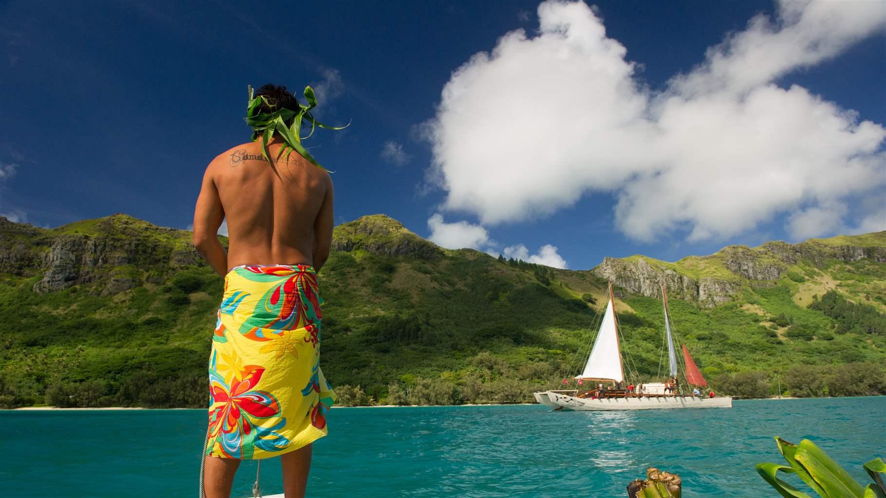 A resident of Raivavae Island looks on as the Fa’afaite, a traditional Polynesian wayfinding canoe, sails in the island’s lagoon.