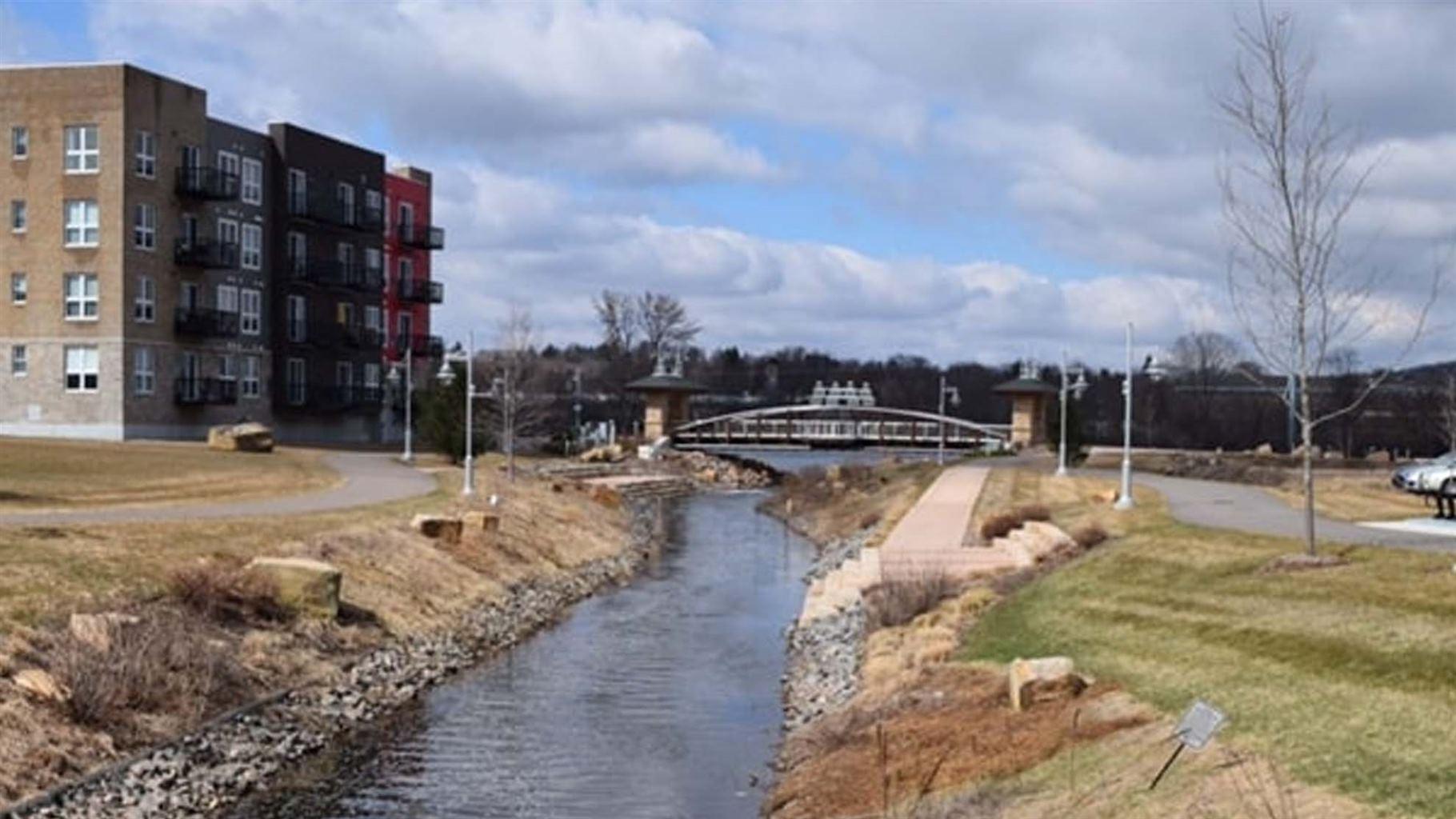 A creek with reinforced banks with a bridge and residential buildings on one side.