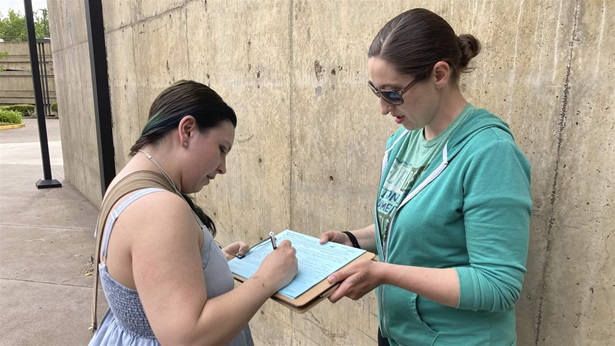 Raevahnna Richardson signs an initiative petition supporting a gun-safety ballot measure on Tuesday, June 7, 2022, outside a library in Salem, Ore., as signature gatherer Rebecca Nobiletti holds the clipboard. 