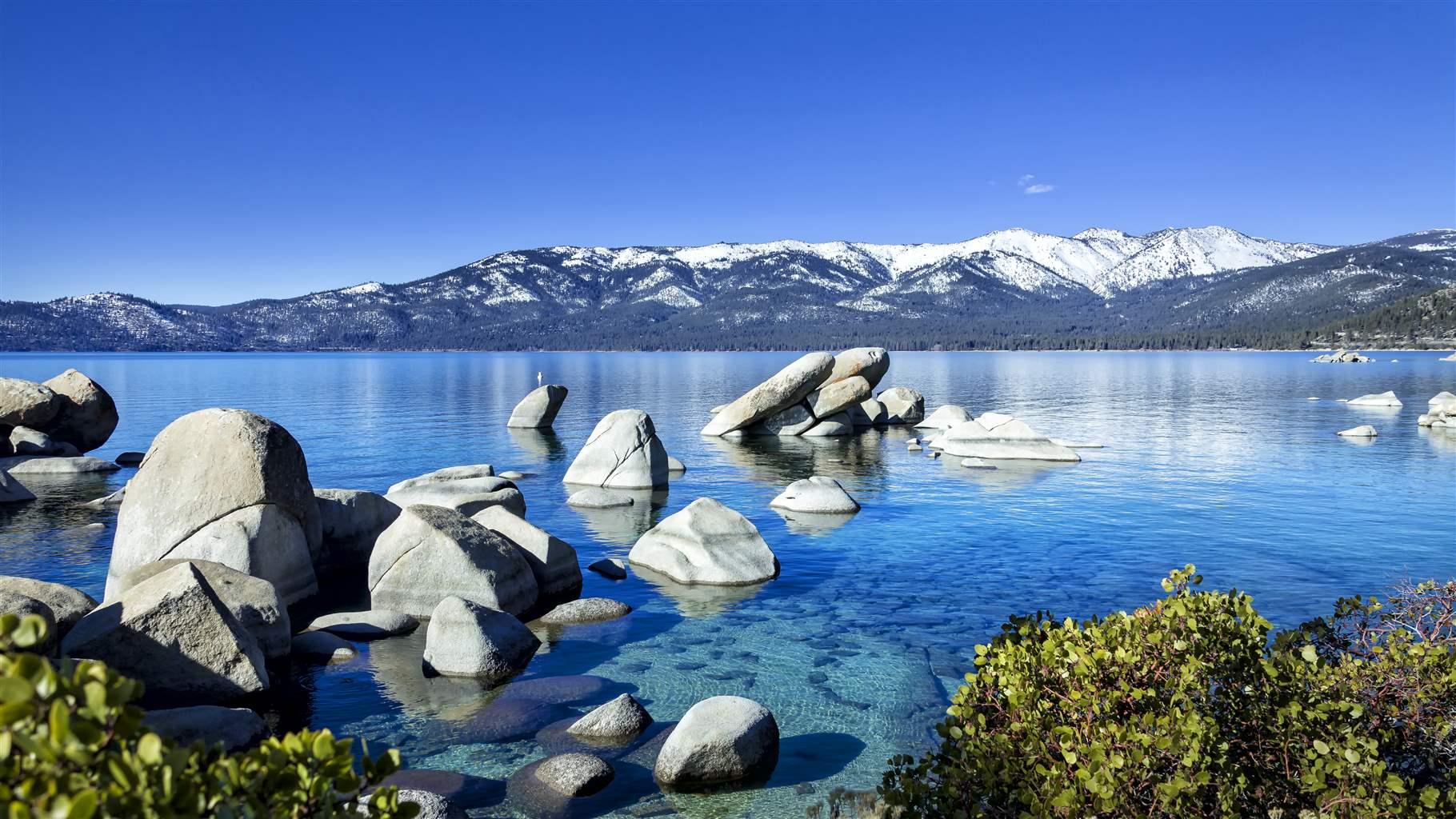 The image is of Sand Harbor, a Neveda State Park located on the Northeast shore of Lake Tahoe in the late winter with lingering snow throughout the park. This location offers some of the most beautiful crystal-clear water with interesting rock formations. The location is a favorite spot for swimming, picnicking, kayaking, boating and even scuba diving.