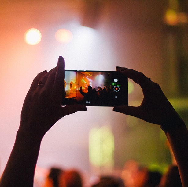 Two hands reaching out from a crowd with a phone to record someone on stage.