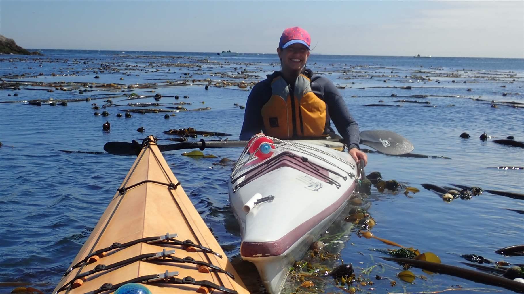A kayaker drifts through across the water speckled with eelgrass as far as the eye can see.