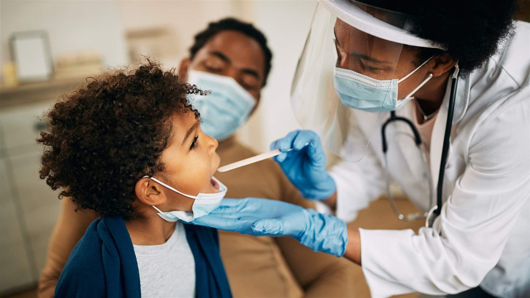 Family doctor examining throat of a small boy