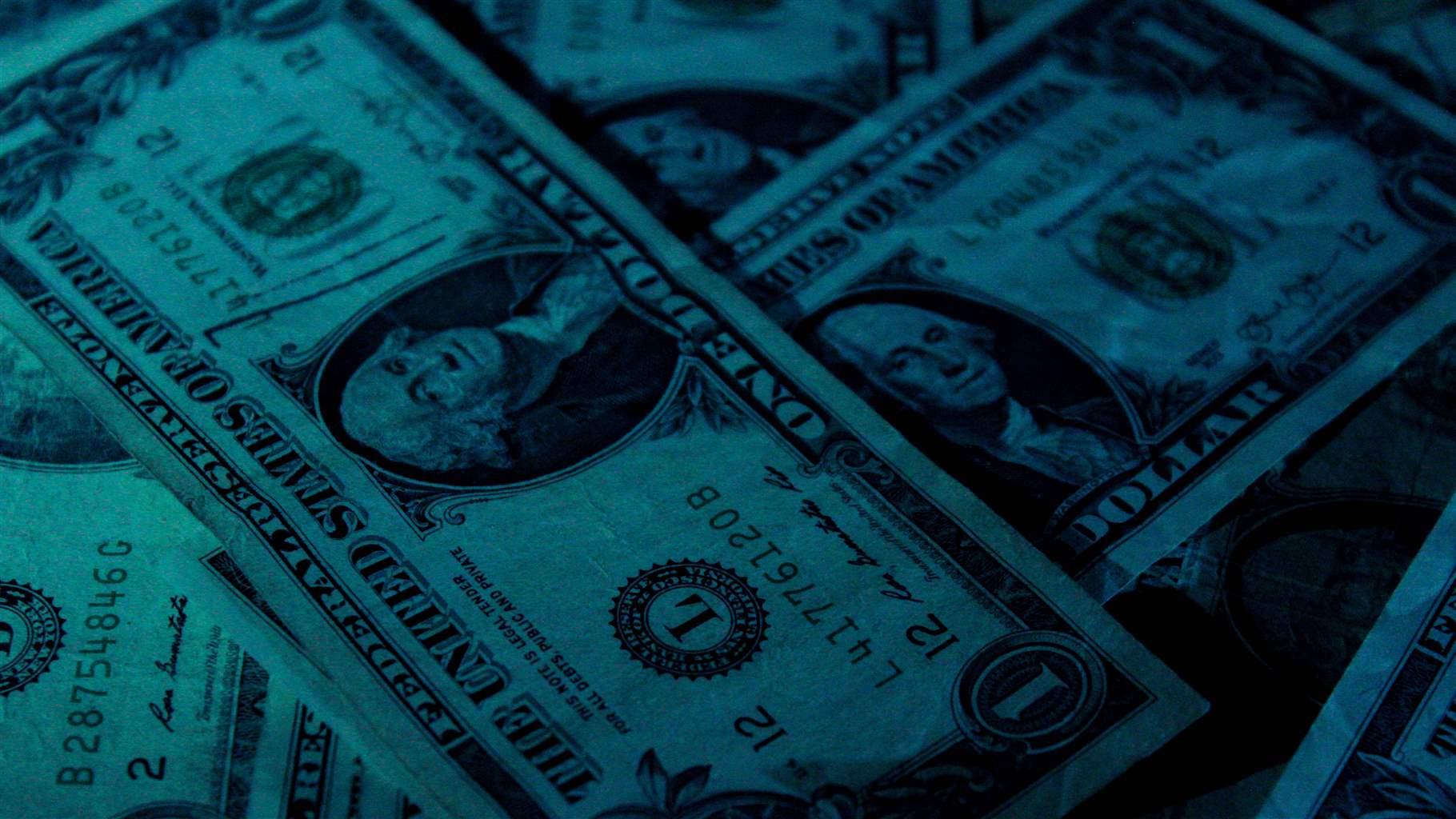 Dollar bills layered and spread out with a blue tint