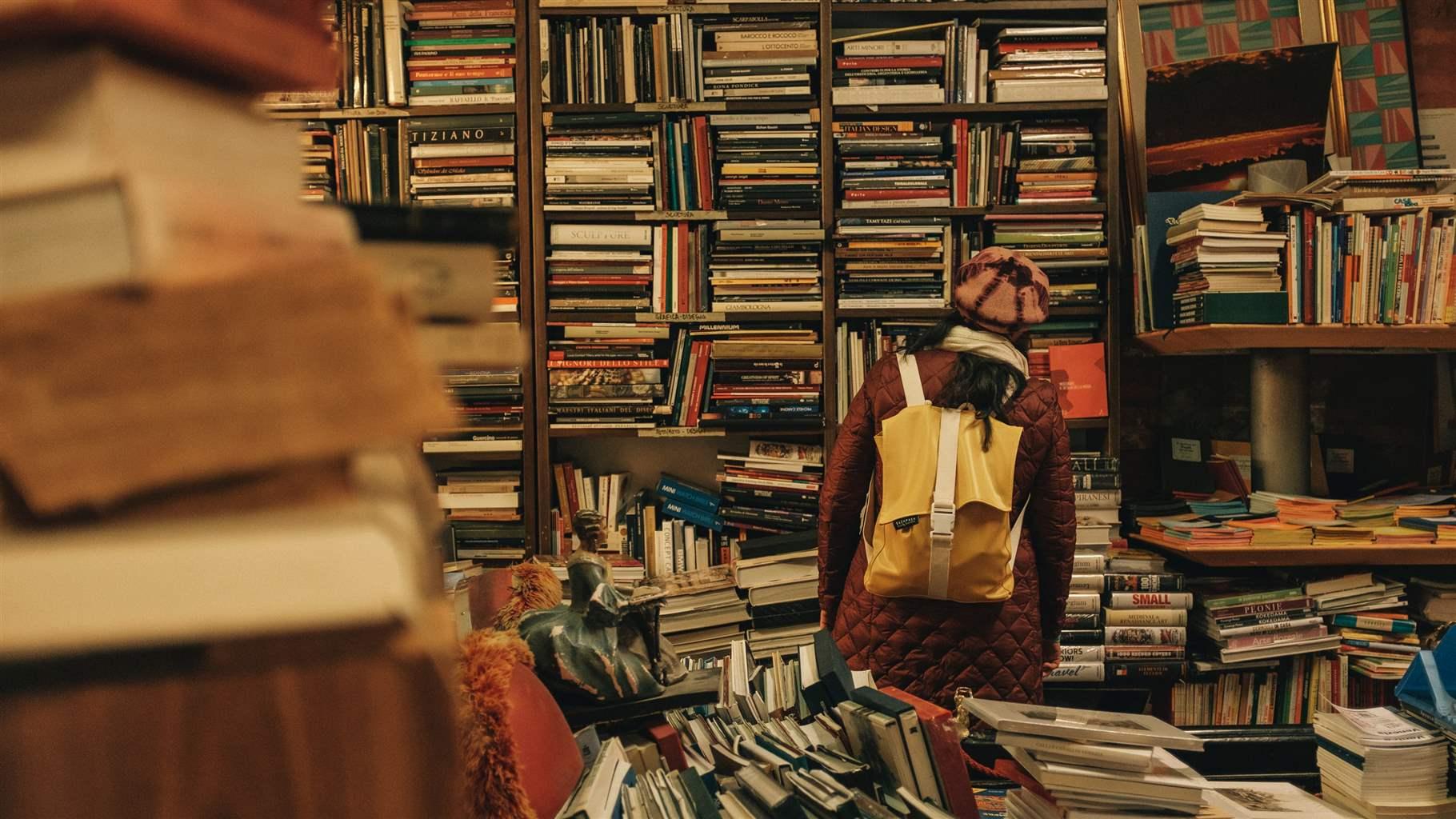 Frontal view of female student's back looking at an array of books at a library