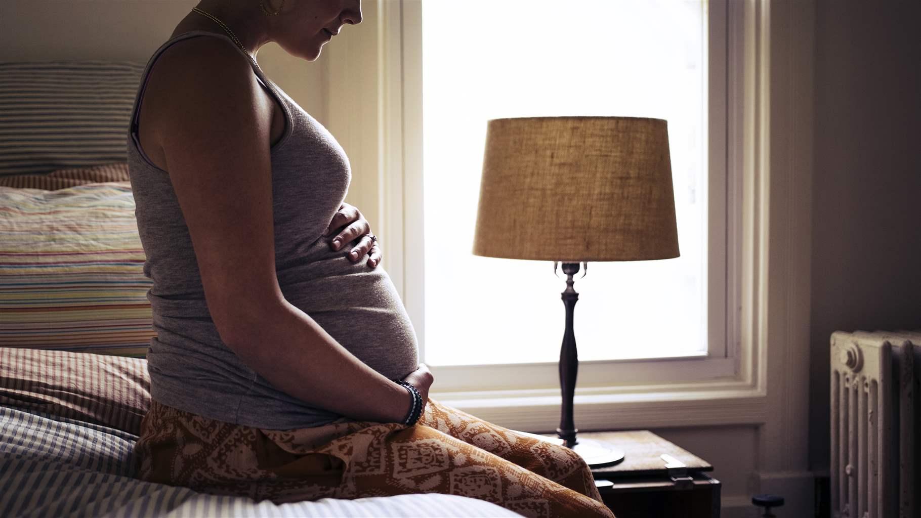 Pregnant young woman sitting on bed at home