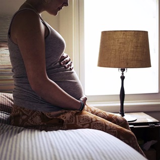 Pregnant young woman sitting on bed at home
