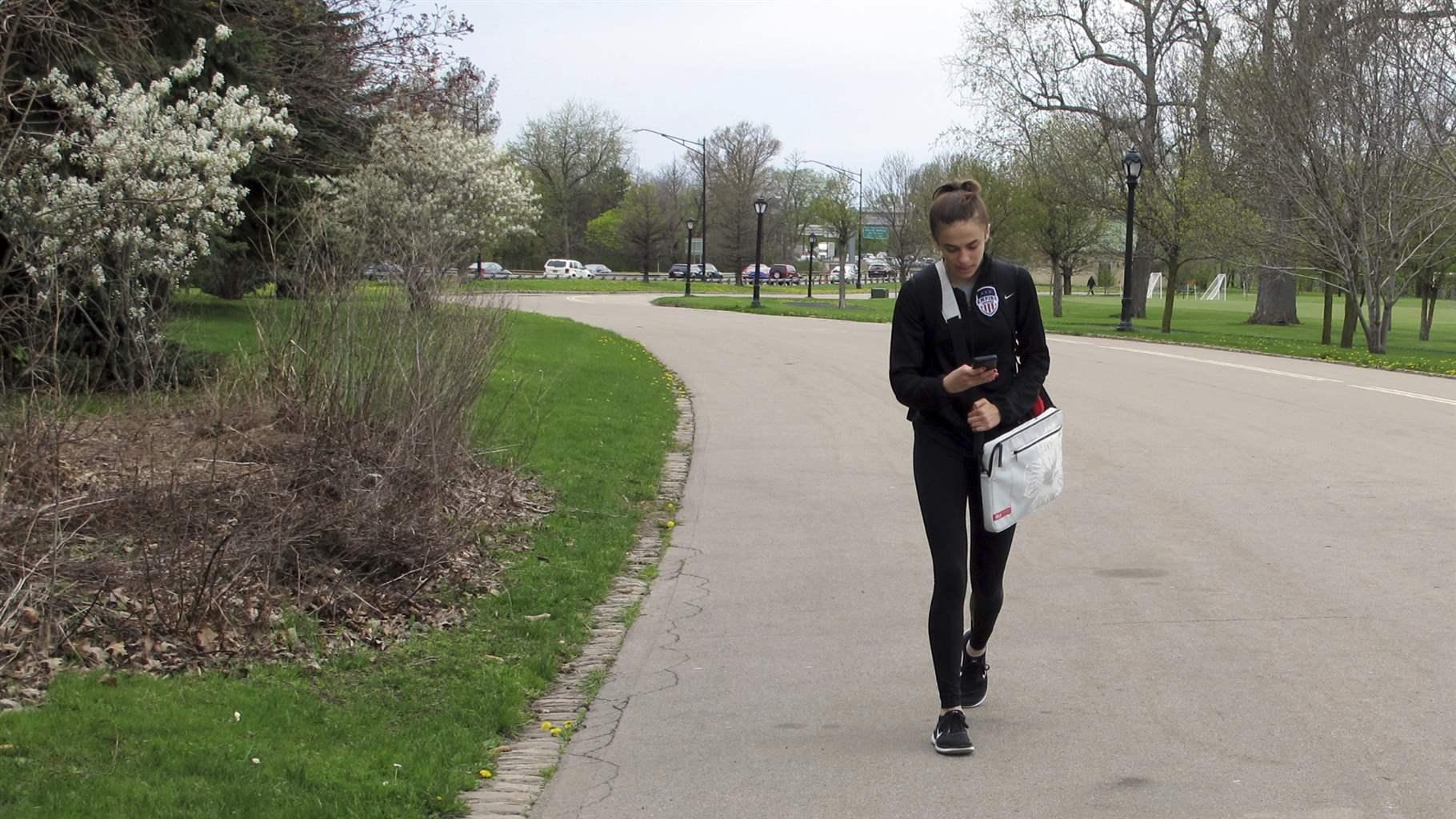 A teenager looks at her cellphone while walking through a park in Buffalo, N.Y.