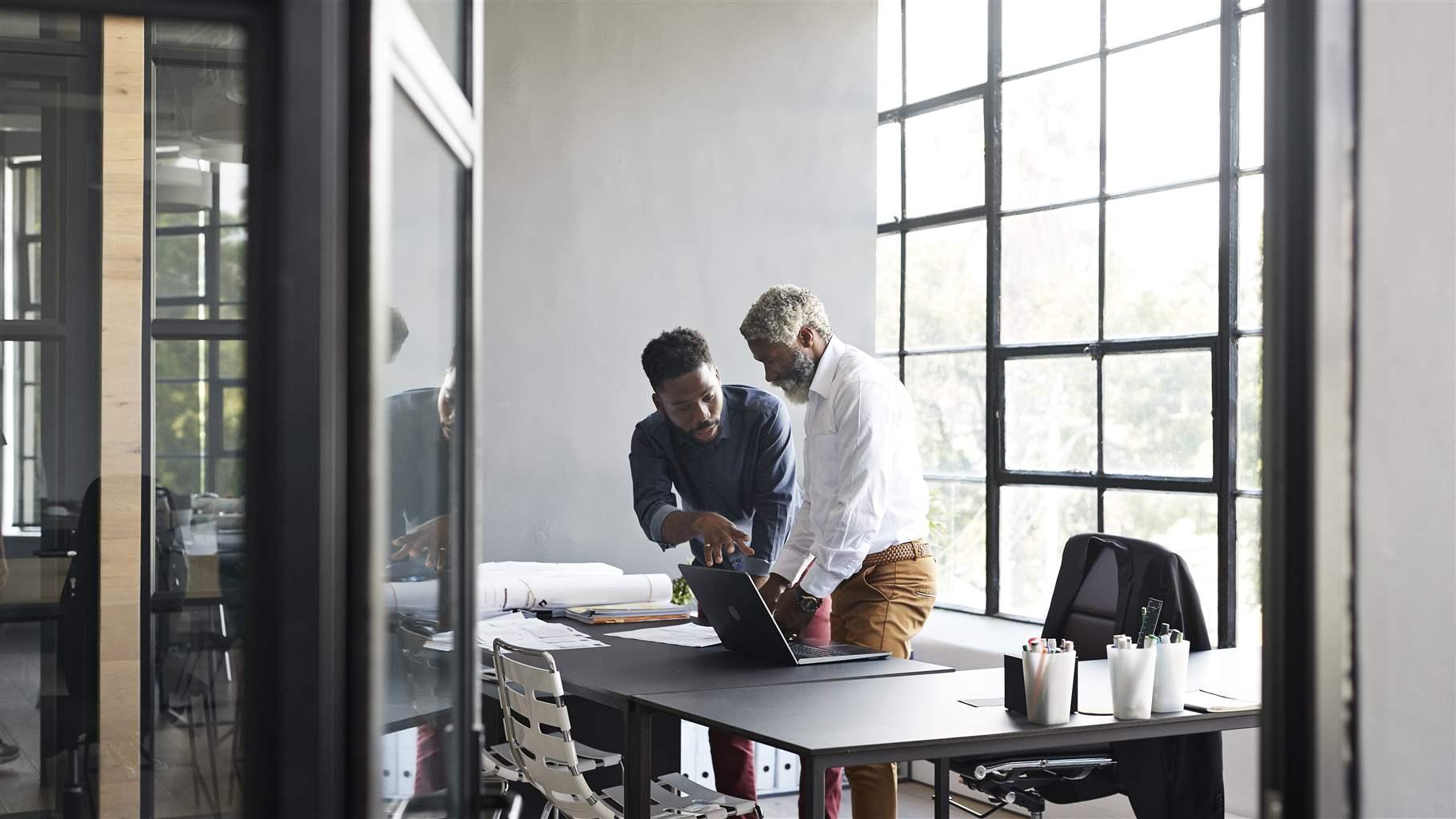 Male entrepreneurs discussing while standing by desk in modern office seen through doorway