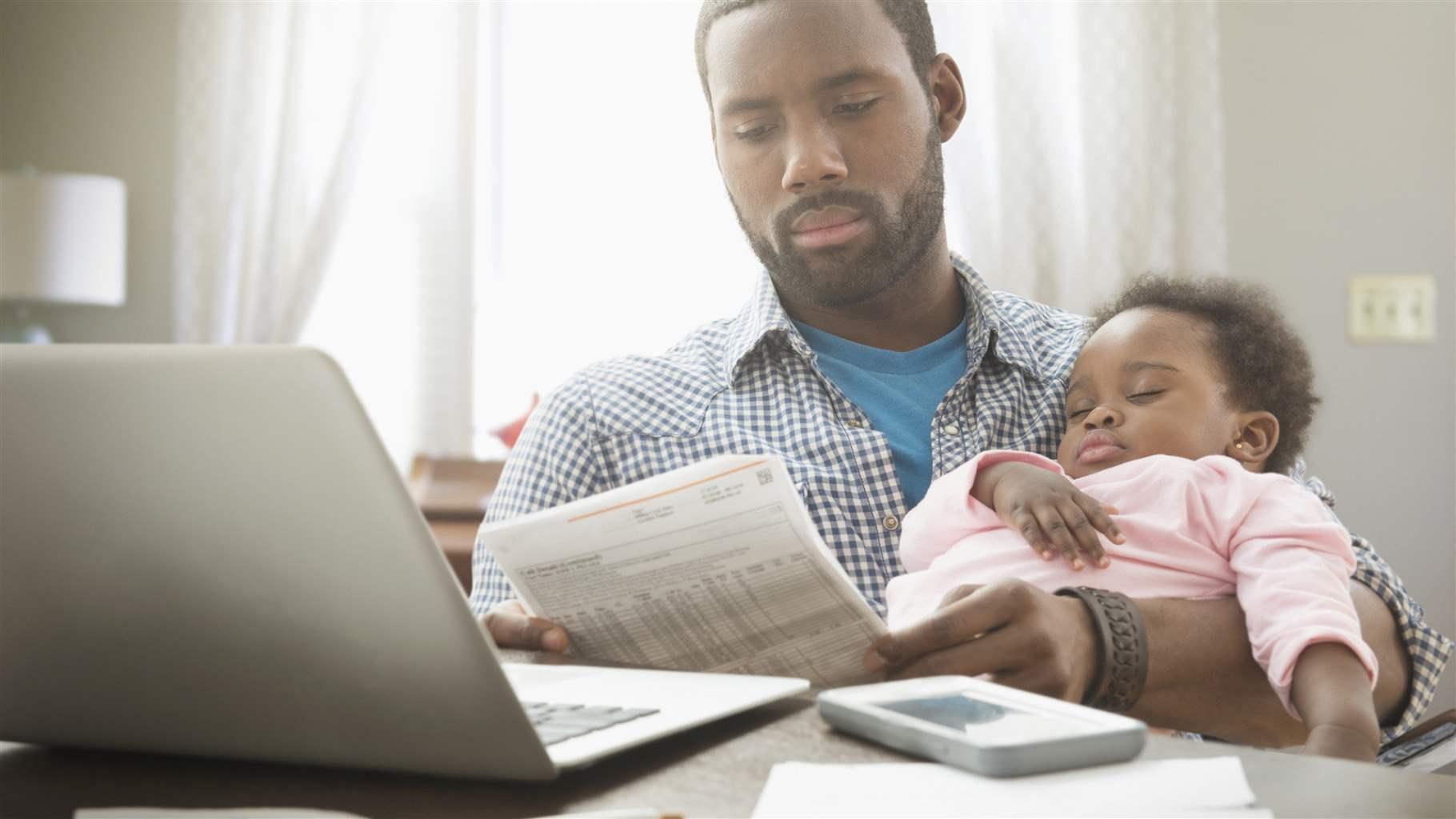Father holding baby daughter and working from home