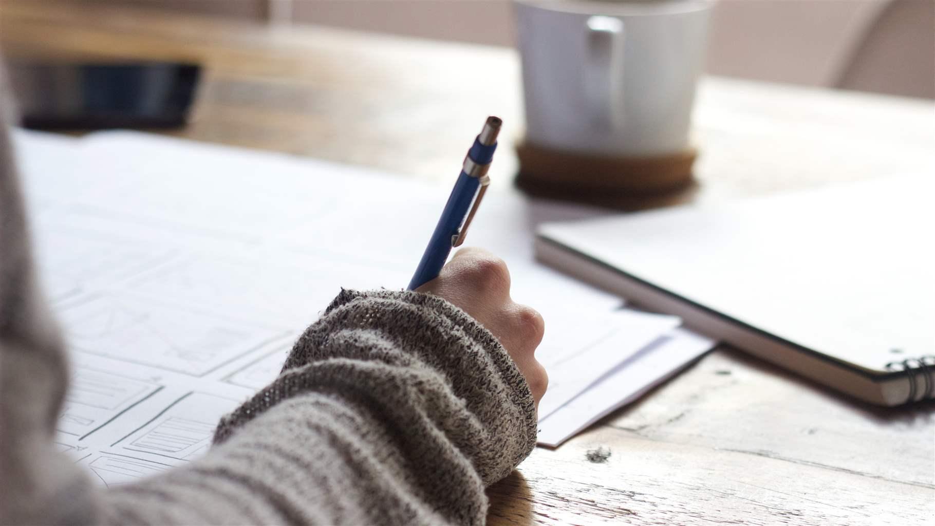 A hand holding a pen with papers laid out on a coffee table