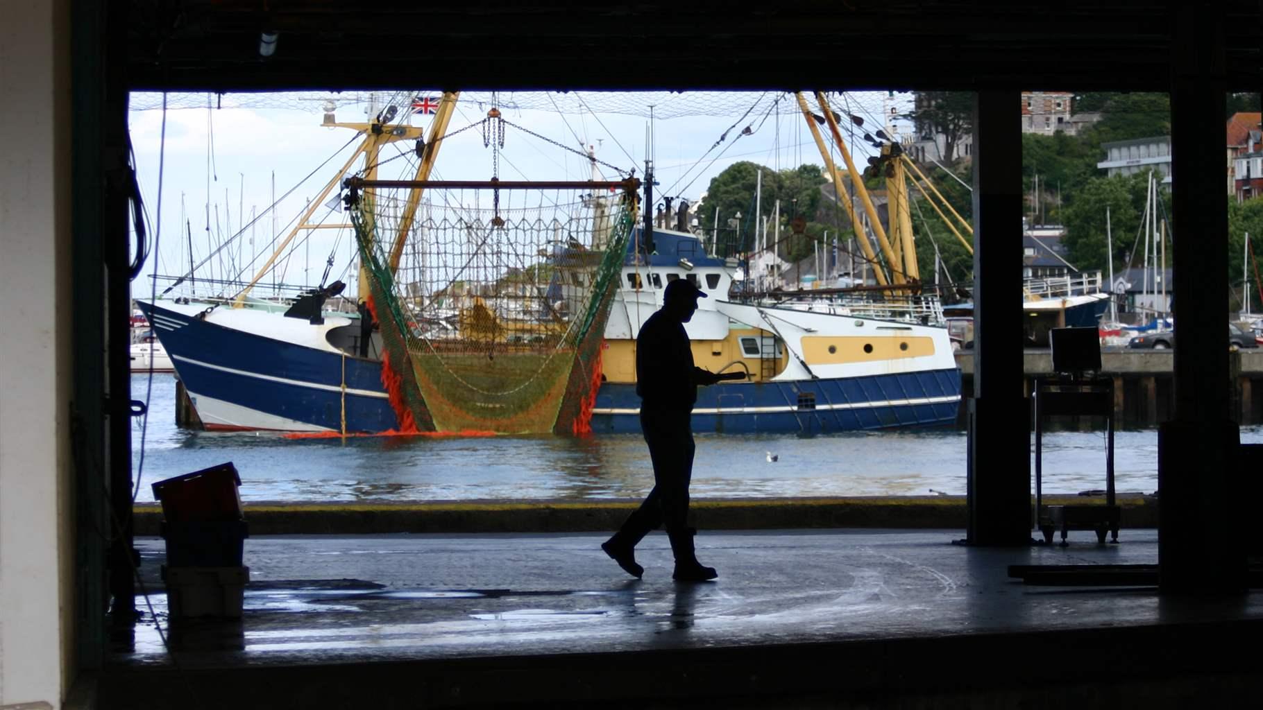 person walking by a fishing boat in a port