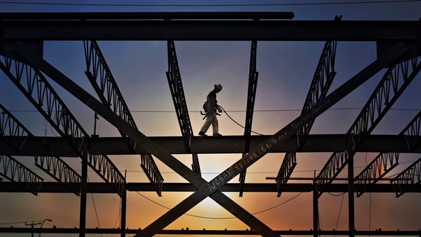 Silhouette of construction worker walking on an I-beam with beautiful sunset sky behind him.