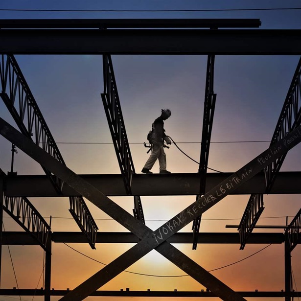 Silhouette of construction worker walking on an I-beam with beautiful sunset sky behind him.