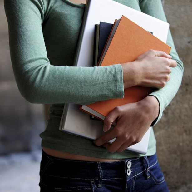 Close up of a female university student holding books and a laptop