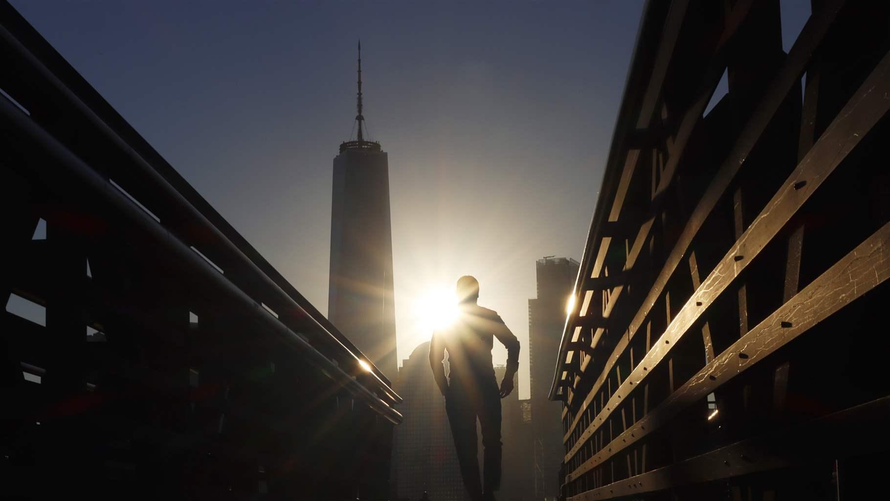 The sun rises behind lower Manhattan and One World Trade Center in New York City as a man walks on a ferry dock on September 20, 2021 in Jersey City, New Jersey. 