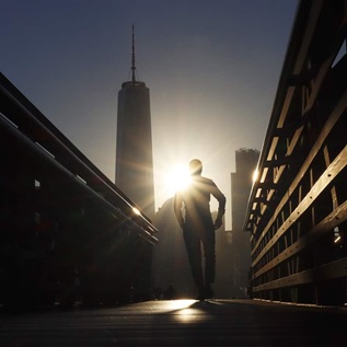 The sun rises behind lower Manhattan and One World Trade Center in New York City as a man walks on a ferry dock on September 20, 2021 in Jersey City, New Jersey. 