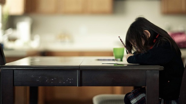 Portrait of a young girl in a private school uniform doing homework at the kitchen table.