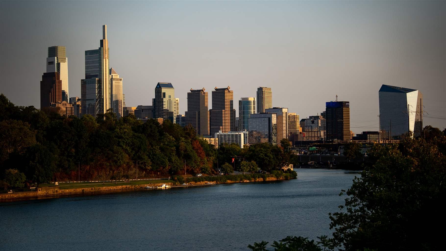 A view of one of Philadelphia’s major rivers in the foreground, framed by tree-lined banks, with the skyscrapers that form the city’s skyline towering in the distance.