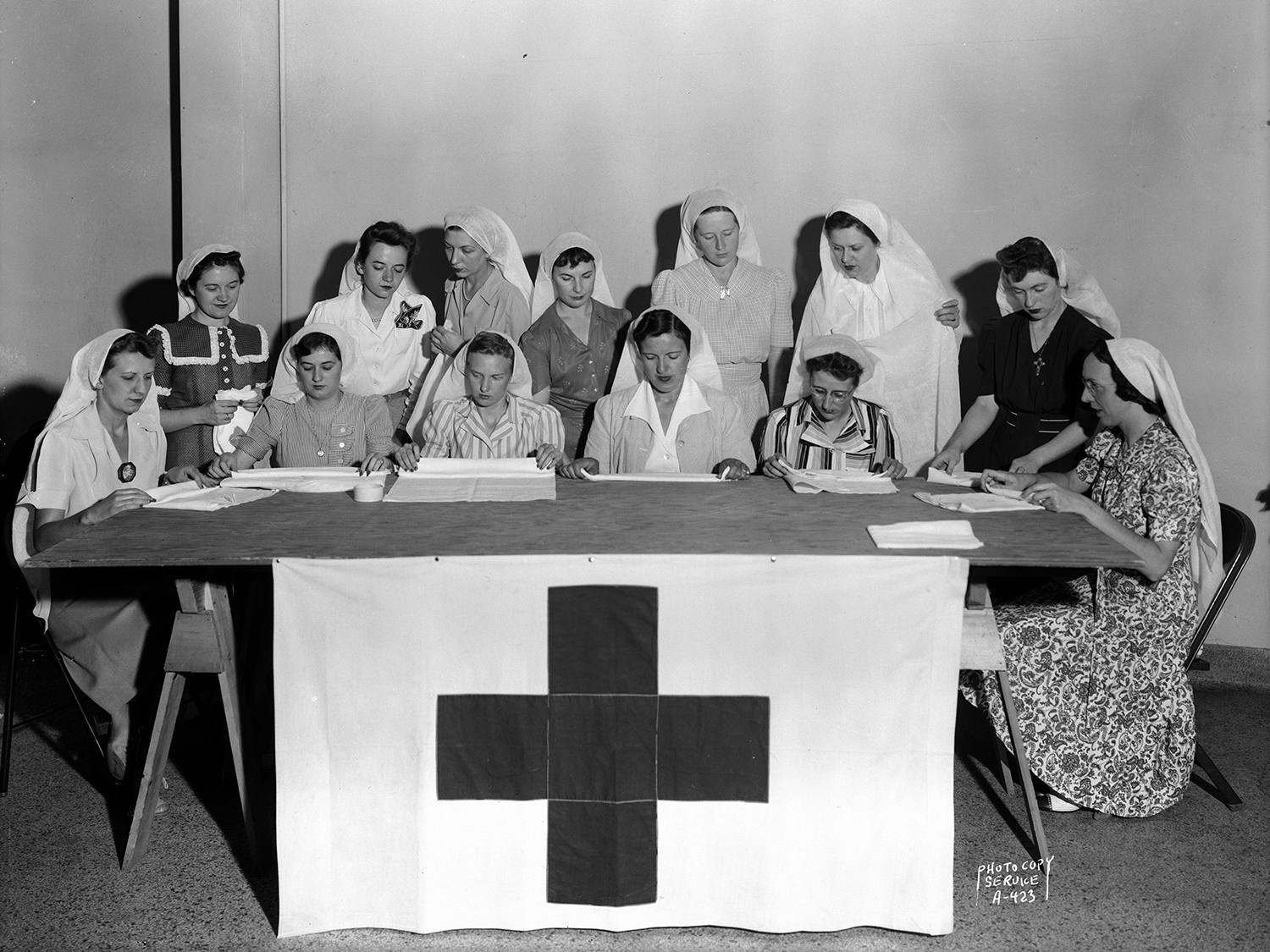 State female employees making surgical dressings / bandages for the American Red Cross in the Wisconsin State Employees Association building, 448 W Washington Avenue, Madison, Wisconsin, August 17, 1942. Seated, l to r: Marion Block, Lenore Hassett, Caroline Dagestad, Lydia Stumpf (leader), Vyrgil Tuft, and Dorothy Ryan. Standing, l to r : Lenore Brownlee, Rosaline Bee, Eulalia Fader, Eleanor DeMerse, Rosella Marshall, Zenobia Peachey and Dorothy Wilhelm.