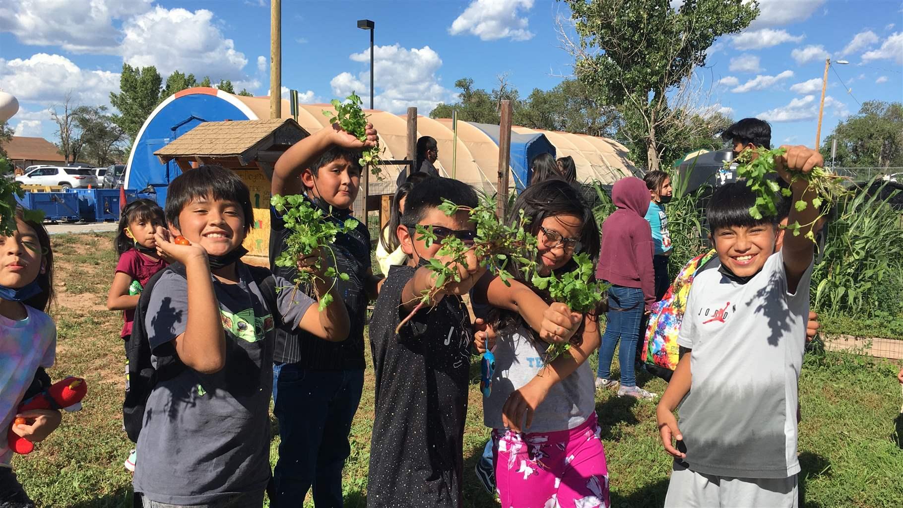 Photo shows children from the Zuni Pueblo in New Mexico holding up foods grown in their community garden.