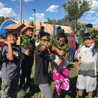 Photo shows children from the Zuni Pueblo in New Mexico holding up foods grown in their community garden.
