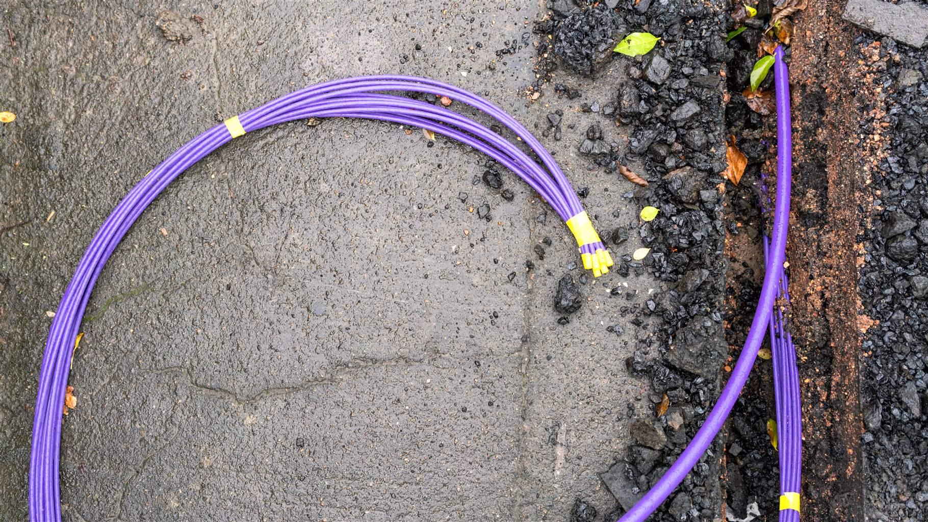 A purple bundle of fibre optic cables during installation under the pavement surface.