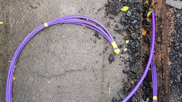 A purple bundle of fibre optic cables during installation under the pavement surface.