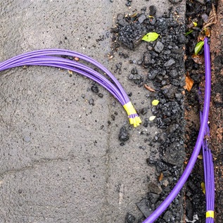 A purple bundle of fibre optic cables during installation under the pavement surface.
