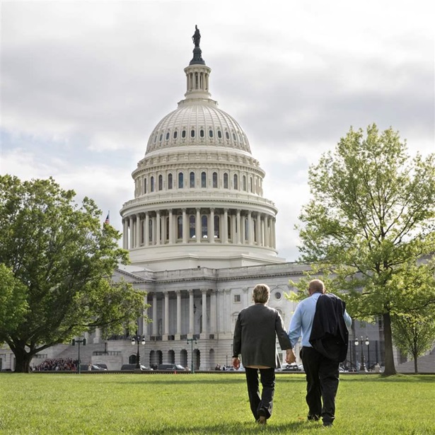 A couple with gray hair hold hands and walk towards the U.S. Capitol building.