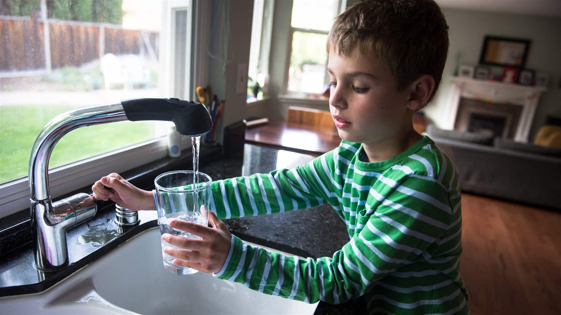 Boy turning off the tap after getting water from the kitchen sink.