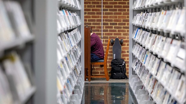 A student sitting at a table at the end of a library stack. 