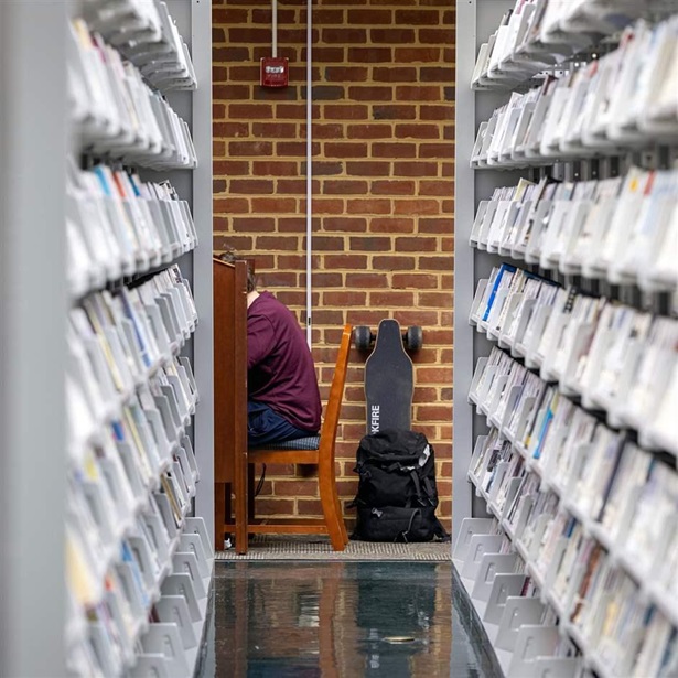 A student sitting at a table at the end of a library stack. 