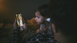A sick child with a man consulting with a doctor through a video call on a smartphone from home.