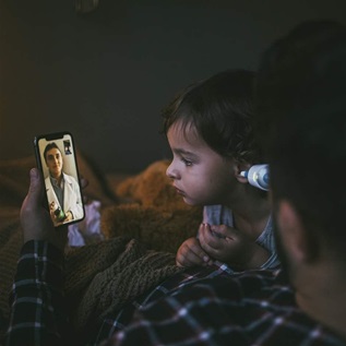 A sick child with a man consulting with a doctor through a video call on a smartphone from home.