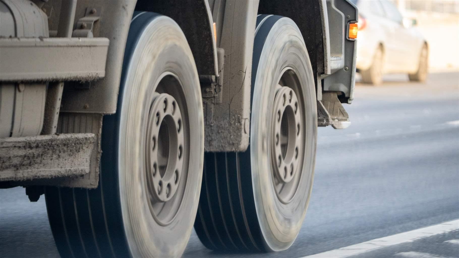 Close-up of two grey lorry wheels in motion on an asphalt road