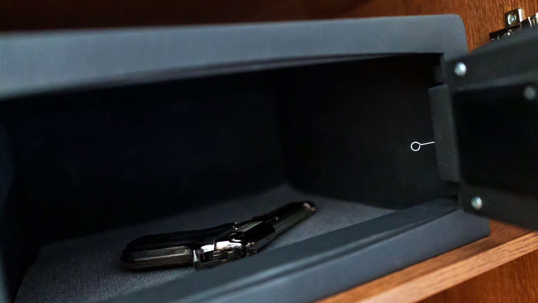  A handgun lies inside an open metal safe on a wooden shelf.