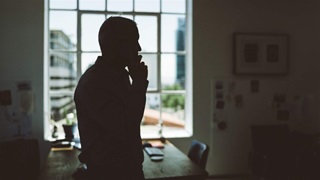 A person stands in front of a bright window holding a cell phone up to their ear.