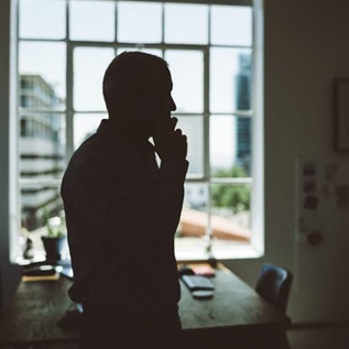 A person stands in front of a bright window holding a cell phone up to their ear.
