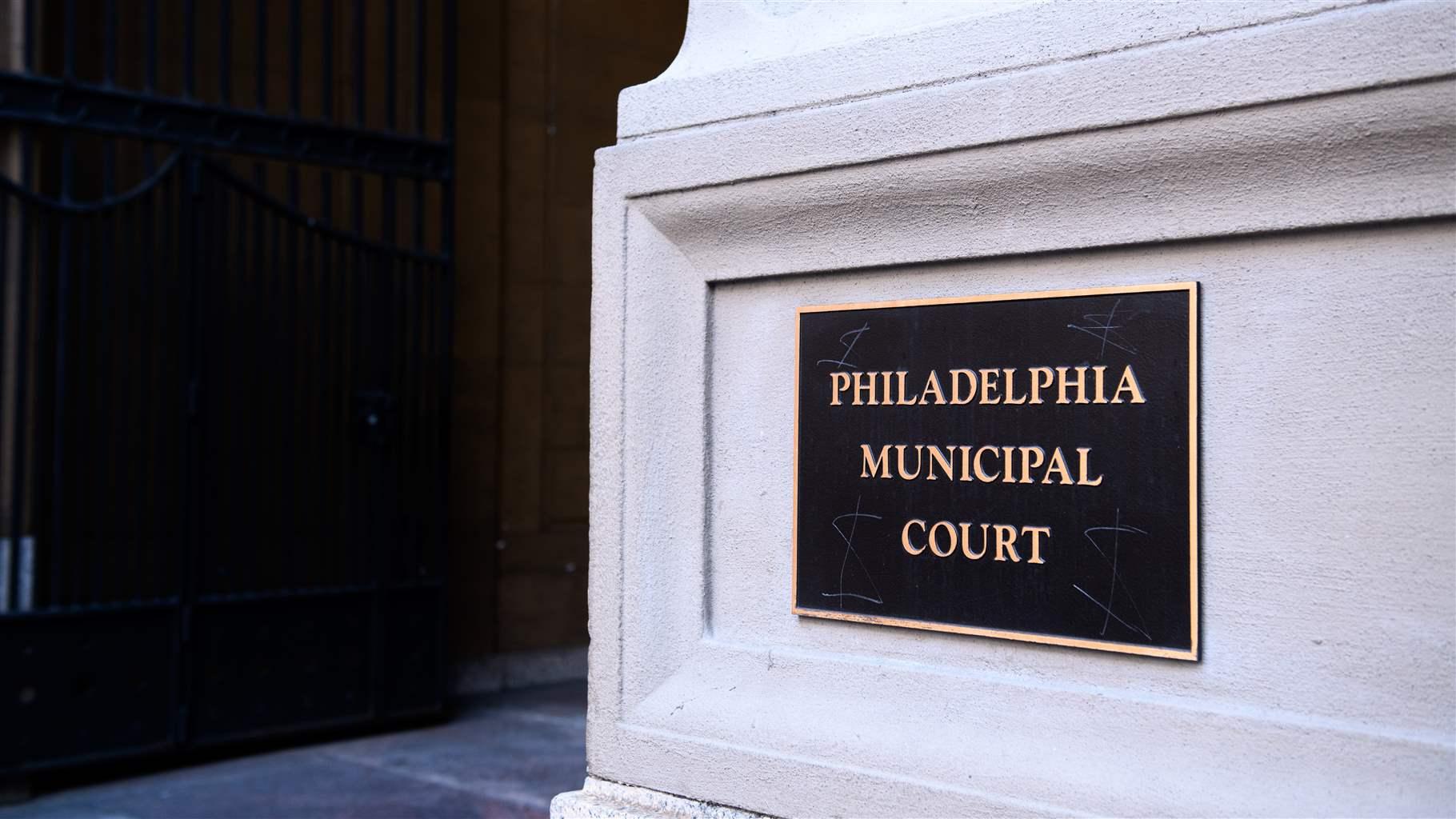 A dark metal plaque with gold letters that read “Philadelphia Municipal Court” is centered on a stone wall next to the court building’s entrance in Center City.