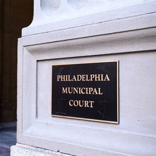 A dark metal plaque with gold letters that read “Philadelphia Municipal Court” is centered on a stone wall next to the court building’s entrance in Center City.
