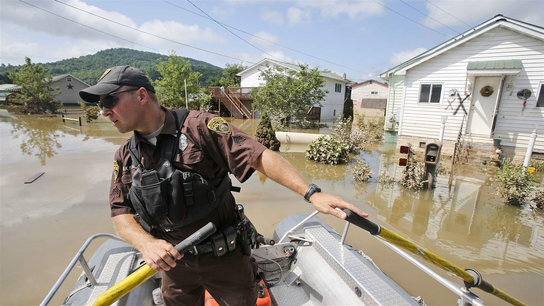 A natural resource officer navigates a small boat past houses on a flooded street.  