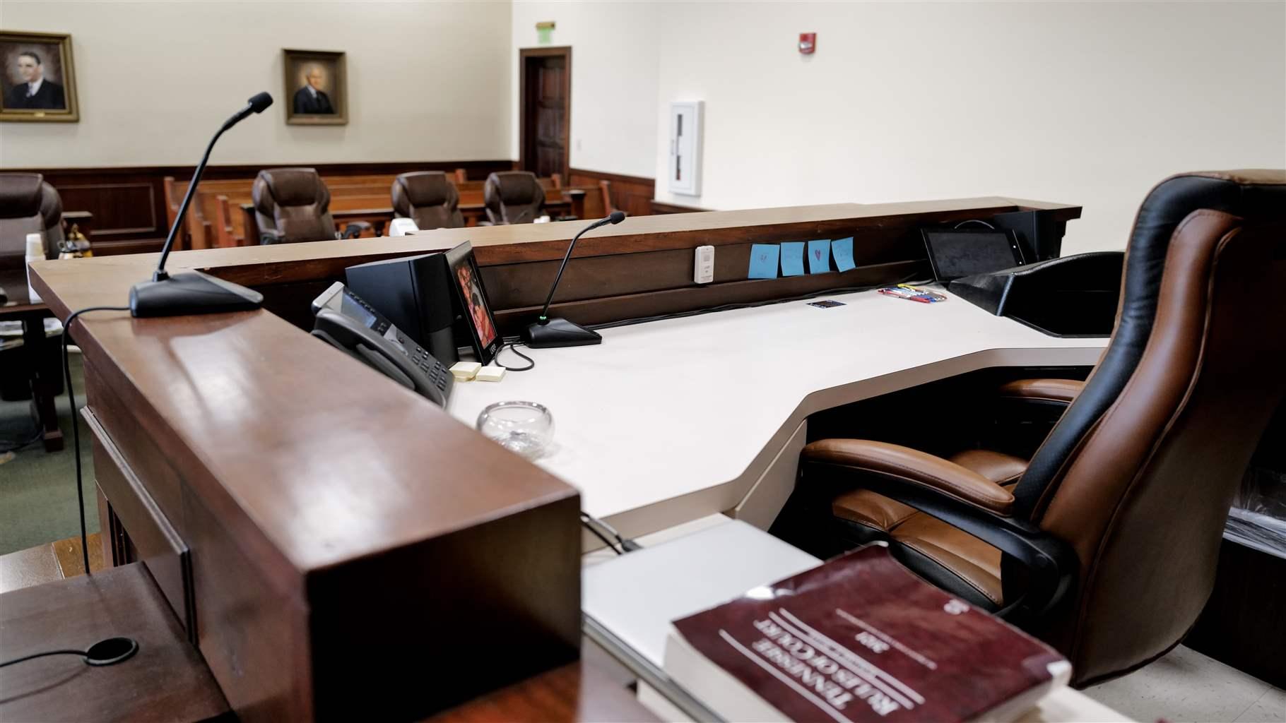 A dark wooden desk overlooks an empty courtroom decorated with several painted portraits.