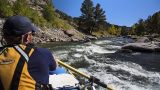A person in a boat navigates a white-crested river with tree-lined canyons on either side. 