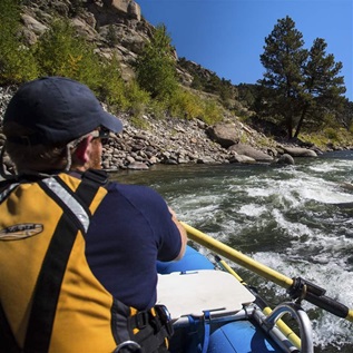 A person in a boat navigates a white-crested river with tree-lined canyons on either side. 