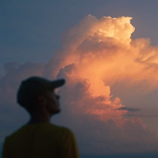 A person in silhouette looks upward at a cloud with sunlight breaking against it.