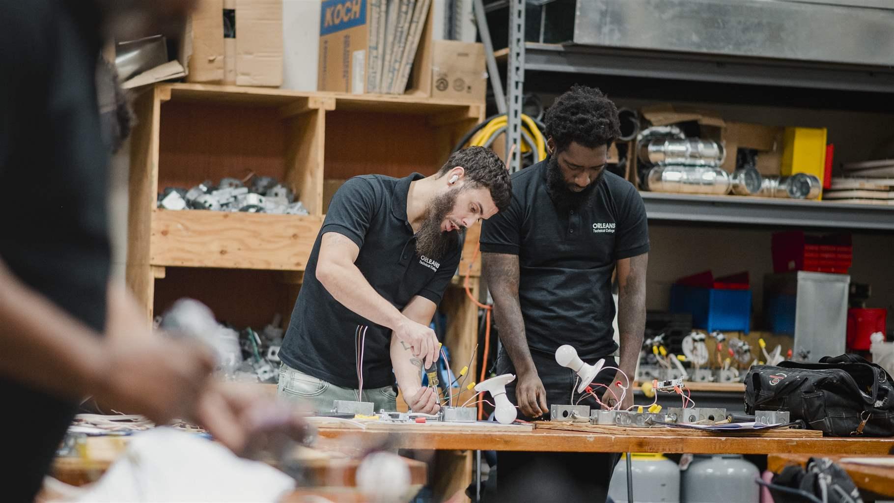 Two people stand behind a wooden work bench, adjusting electrical wiring.