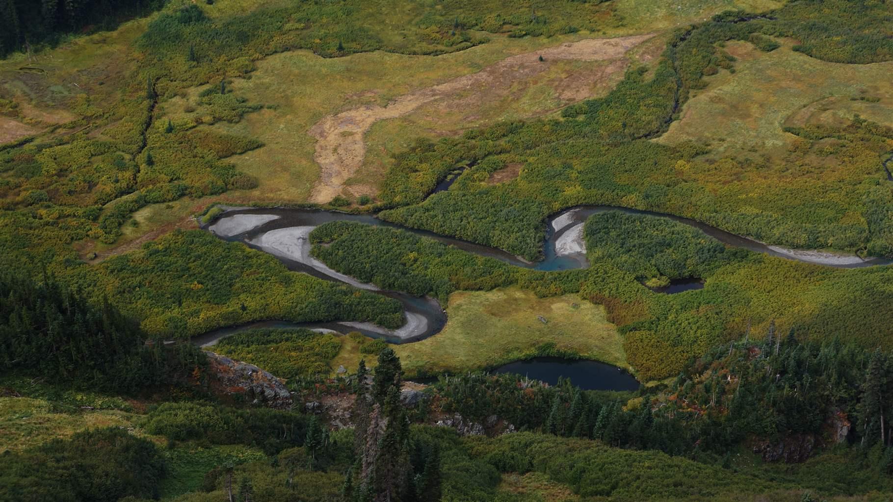 An aerial photo shows a river snaking through hilly, green, undeveloped terrain.