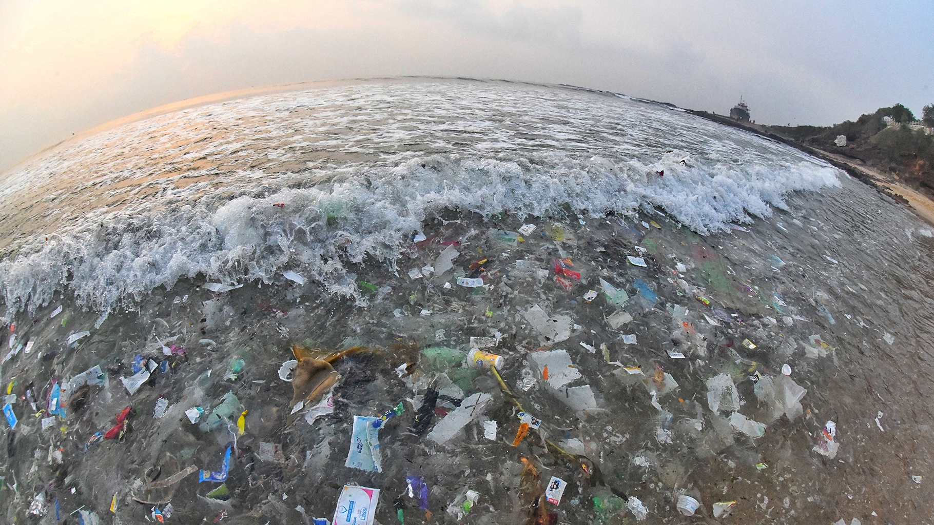 A wide angle lens shot of waves filled with trash crashing on beach.