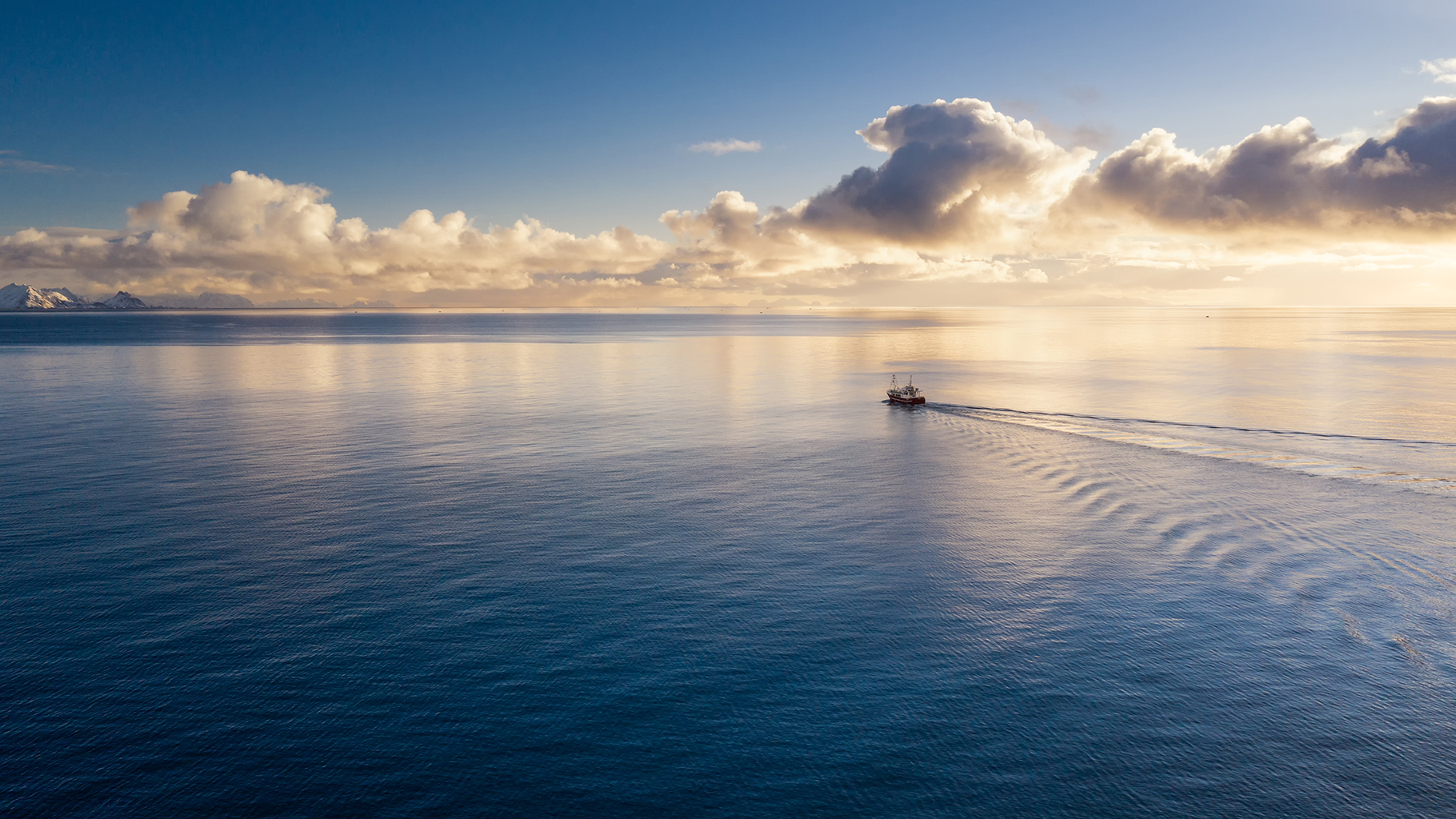 A lone ship at sea with fluffy white clouds in the distance. 